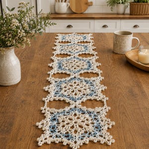 May include: A long, rectangular crochet table runner featuring a repeating pattern of interconnected floral motifs. The design is crafted from cream-colored yarn with accents of light blue thread woven into the center of each circular element.