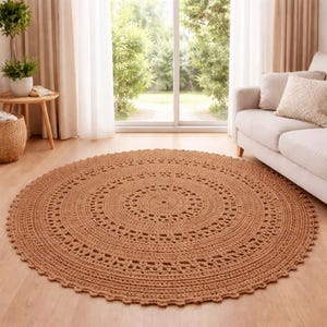 May include: A circular, crocheted rug in a warm brown colour. The rug has a detailed, circular pattern and a scalloped edge. It is placed on a wooden floor in a well-lit room, near a window and a sofa.