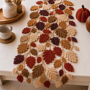 May include: A crochet table runner featuring a cascading vine design with numerous oak leaves in shades of cream, tan, brown, rust, and deep burgundy. The leaves are connected by a central crocheted vine structure, creating a textured autumn display.