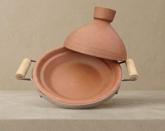 May include: A terracotta tagine pot with a conical lid, set on a metal base with wooden handles. The open pot reveals its interior. The tagine is a traditional cooking vessel used in North African cuisine.
