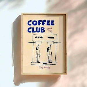 May include: Framed art print featuring the words "COFFEE CLUB" in blue, and "Served Daily" above a coffee machine illustration. Two figures are depicted looking up at the machine. The words "Every Morning" are written below.