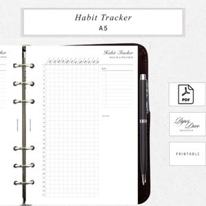 May include: A white A5 habit tracker insert with a grid layout for tracking habits. The insert includes the text "Habit Tracker" and "Health & Wellness". A black pen rests on the right side. The insert is inside a dark brown leather binder.