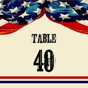 Op de afbeelding: Een rood, wit en blauwe Amerikaanse vlag met sterren hangt boven een witte kaart met de tekst "TABLE 40" in zwart.