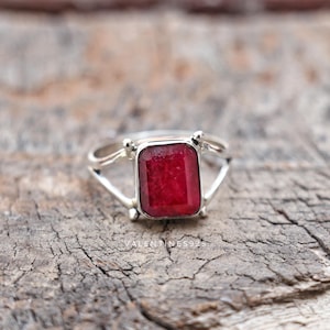 Könnte beinhalten: Ein Silberring mit einem rechteckigen, tiefroten Edelstein in einer Vier-Krappen-Fassung und einer geteilten Ringschiene. Der Text VALENTINES925 ist an der Basis des Rings sichtbar, der ein poliertes Metallfinish und einen facettierten Stein aufweist.