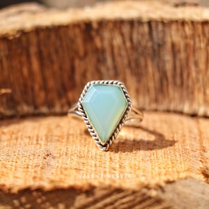 May include: A silver ring featuring a kite-shaped, pale blue-green gemstone set within a twisted rope-style metal border. The band is smooth and metallic. The text VALENTINES925 is visible at the base of the ring setting.