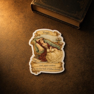 May include: A die-cut sticker featuring a vintage-style illustration of a person in a red dress reclining on a teal sofa while reading a book. The sticker includes the text Tragic. at the top and once again undone by my own lack of follow-through at the bottom.