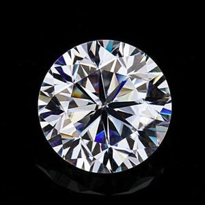 May include: A round brilliant cut gemstone with a clear, colourless appearance. The stone features numerous triangular and kite-shaped facets that create a complex geometric pattern, reflecting light with sharp contrast against a black background.