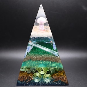 May include: A layered pyramid-shaped resin art piece. The pyramid features a clear top with a mushroom, and various layers of green, brown, and blue materials. The base has copper-colored spirals and a dark blue hue.