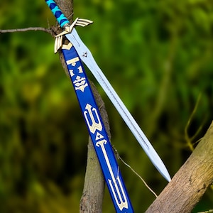 May include: A silver-colored metal sword with a gold-toned crossguard and a blue-wrapped handle. The sword is accompanied by a blue scabbard featuring gold-colored geometric symbols and a gold-toned metal tip, resting against a textured tree branch.
