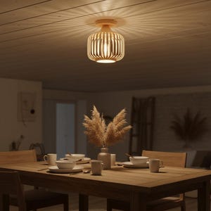 Könnte beinhalten: Eine Deckenleuchte aus Holz mit einem zylindrischen Schirm aus vertikalen Holzlatten. Das Licht ist eingeschaltet und wirft einen warmen Schein. Die Leuchte ist an einer hellen Holzdecke montiert. Der Raum verfügt über einen Esstisch aus Holz.
