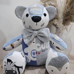 May include: A patchwork teddy bear in blue, white, and grey. The bear has a bow tie, corduroy ears, and a black nose. The word "CUTE" is visible on the bear's body, with a zebra and penguin design on the feet. A charming handmade toy.
