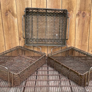 May include: Three metal wire baskets with a rustic finish. The baskets are rectangular and have a diamond-shaped wire mesh. The baskets are stacked on top of each other.