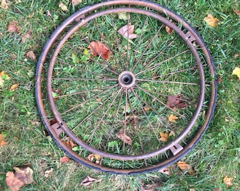 May include: A rusty metal wheel with a black tire, lying on a bed of green grass and brown leaves.
