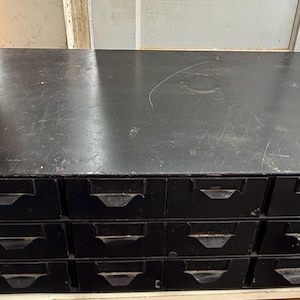 May include: A black, vintage-style cabinet with multiple drawers. The cabinet has a rectangular shape and a flat top. Each drawer has a metal handle. The cabinet appears to be made of wood and has a distressed finish.