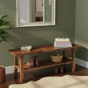 Puede incluir: Un banco de madera con un estante inferior, que contiene libros, una cesta de mimbre y botas. El banco es de madera oscura y tiene un acabado natural. Un espejo con marco blanco cuelga de la pared verde sobre el banco.
