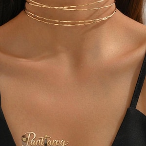 Op de afbeelding: Een goudkleurige choker ketting met drie fijne, golvende strengen. De ketting heeft een minimalistisch ontwerp, perfect om te combineren of alleen te dragen. De sieraden zijn een stijlvol accessoire.