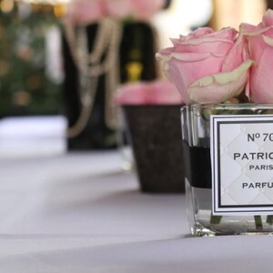 May include: A clear glass jar with a black ribbon around the top, filled with pink roses. The jar has a white label with black text that reads "N&deg; 70 PATRIC PARIS PARFUM".