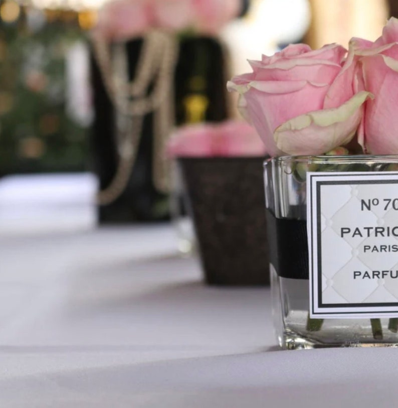 May include: A clear glass jar with a black ribbon around the top, filled with pink roses. The jar has a white label with black text that reads "N&deg; 70 PATRIC PARIS PARFUM".