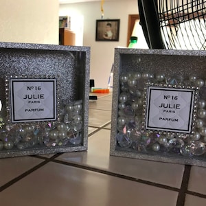 May include: Two silver glitter picture frames with a white label that reads "N&deg; 16 JULIE PARIS PARFUM" and are filled with white pearls and iridescent rhinestones.