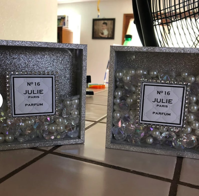May include: Two silver glitter picture frames with a white label that reads "N&deg; 16 JULIE PARIS PARFUM" and are filled with white pearls and iridescent rhinestones.