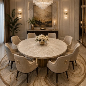May include: A round dining table with a textured white stone surface and a gold pedestal base, surrounded by eight beige upholstered chairs with quilted backs and gold ring accents, positioned beneath a tiered crystal and gold chandelier.