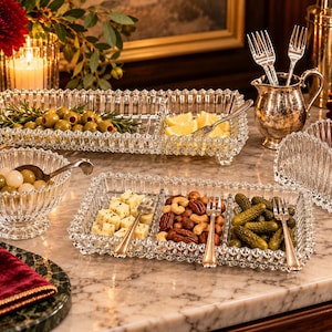 May include: A collection of clear pressed glass serving pieces including two rectangular divided trays, a round footed bowl, and an arched napkin holder. The set features a faceted geometric pattern and is accompanied by small silver-toned metal forks.