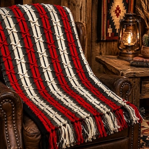 May include: A rectangular knit throw blanket featuring a repeating vertical pattern of red, charcoal gray, and cream stripes with a textured cable-knit design. The blanket is finished with long, multi-colored fringe tassels along the bottom edge.