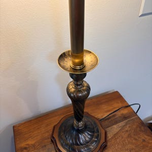 Puede incluir: Una l&aacute;mpara de mesa de estilo vintage con una base de bronce oscuro y un v&aacute;stago de color lat&oacute;n. La l&aacute;mpara presenta un dise&ntilde;o decorativo y ornamentado y se asienta sobre una base de madera. La l&aacute;mpara est&aacute; enchufada a una toma de corriente.