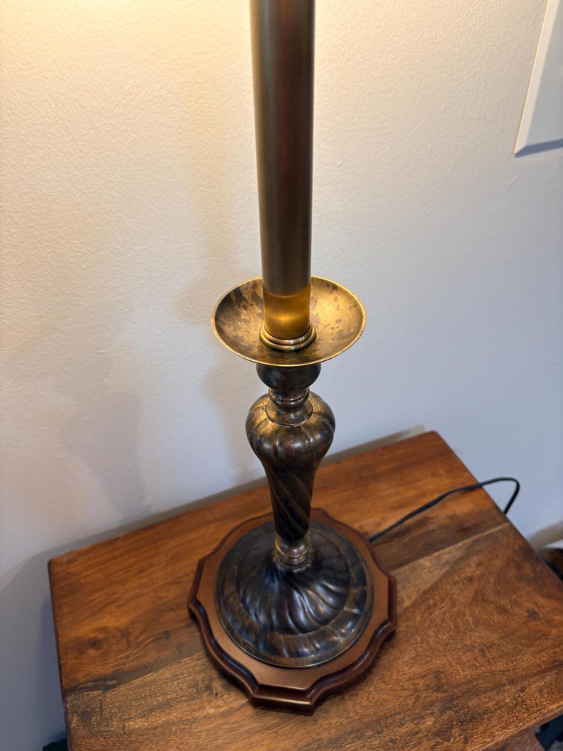 Puede incluir: Una l&aacute;mpara de mesa de estilo vintage con una base de bronce oscuro y un v&aacute;stago de color lat&oacute;n. La l&aacute;mpara presenta un dise&ntilde;o decorativo y ornamentado y se asienta sobre una base de madera. La l&aacute;mpara est&aacute; enchufada a una toma de corriente.