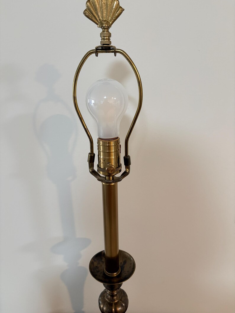Puede incluir: Una l&aacute;mpara de mesa de lat&oacute;n vintage con un remate en forma de concha. La l&aacute;mpara presenta una bombilla, un largo v&aacute;stago de lat&oacute;n y una base decorativa. El dise&ntilde;o de la l&aacute;mpara es cl&aacute;sico y elegante.