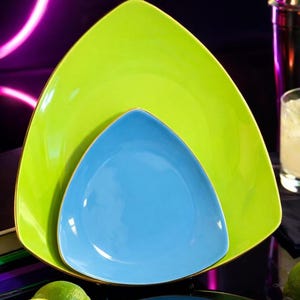 May include: A nested set of three triangular plates. The largest plate is a bright green with a gold rim, the middle plate is a light blue, and the smallest plate is a darker blue. Limes are in the foreground.