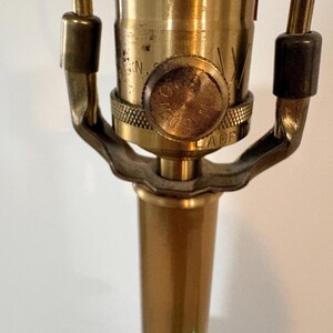 Puede incluir: Primer plano de una base y un casquillo de l&aacute;mpara de lat&oacute;n vintage. La l&aacute;mpara presenta un acabado dorado con una base texturizada y un interruptor giratorio. El dise&ntilde;o de la l&aacute;mpara es cl&aacute;sico y elegante.