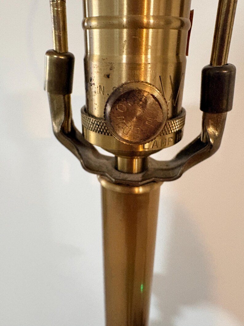 Puede incluir: Primer plano de una base y un casquillo de l&aacute;mpara de lat&oacute;n vintage. La l&aacute;mpara presenta un acabado dorado con una base texturizada y un interruptor giratorio. El dise&ntilde;o de la l&aacute;mpara es cl&aacute;sico y elegante.