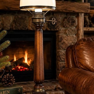 May include: A vintage-style table lamp with a white glass shade and a dark wooden base. The lamp features a decorative metal fixture and a detailed wooden column. The background includes a fireplace with a burning fire, books, and a leather armchair.