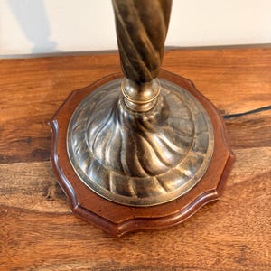 Puede incluir: Una l&aacute;mpara de mesa vintage con una columna retorcida de color lat&oacute;n y una base decorativa. La base presenta un borde de madera oscura y un centro met&aacute;lico. La l&aacute;mpara est&aacute; dise&ntilde;ada para colocarse sobre una mesa u otra superficie plana.