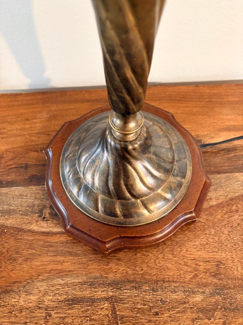 Puede incluir: Una l&aacute;mpara de mesa vintage con una columna retorcida de color lat&oacute;n y una base decorativa. La base presenta un borde de madera oscura y un centro met&aacute;lico. La l&aacute;mpara est&aacute; dise&ntilde;ada para colocarse sobre una mesa u otra superficie plana.