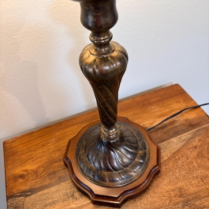 Puede incluir: Un candelero antiguo de lat&oacute;n con un dise&ntilde;o de tallo retorcido. El candelero se asienta sobre una base de madera con un borde decorativo. La parte superior del candelero tiene un plato circular para sostener una vela.
