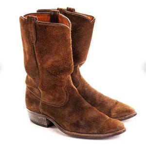 May include: A pair of brown suede cowboy boots. The boots have a classic Western design with a pointed toe, a mid-height shaft, and a stacked heel. The suede has a textured appearance and a warm, earthy tone.
