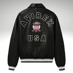 K&ouml;nnte beinhalten: Schwarze Lederjacke mit wei&szlig;en Zierleisten an den Manschetten und am Bund. Auf dem R&uuml;cken steht in wei&szlig;en Blockbuchstaben das Wort "AVIREX" und ein Aufn&auml;her mit "ALL AMERICANS ESTABLISHED 1975 USA".