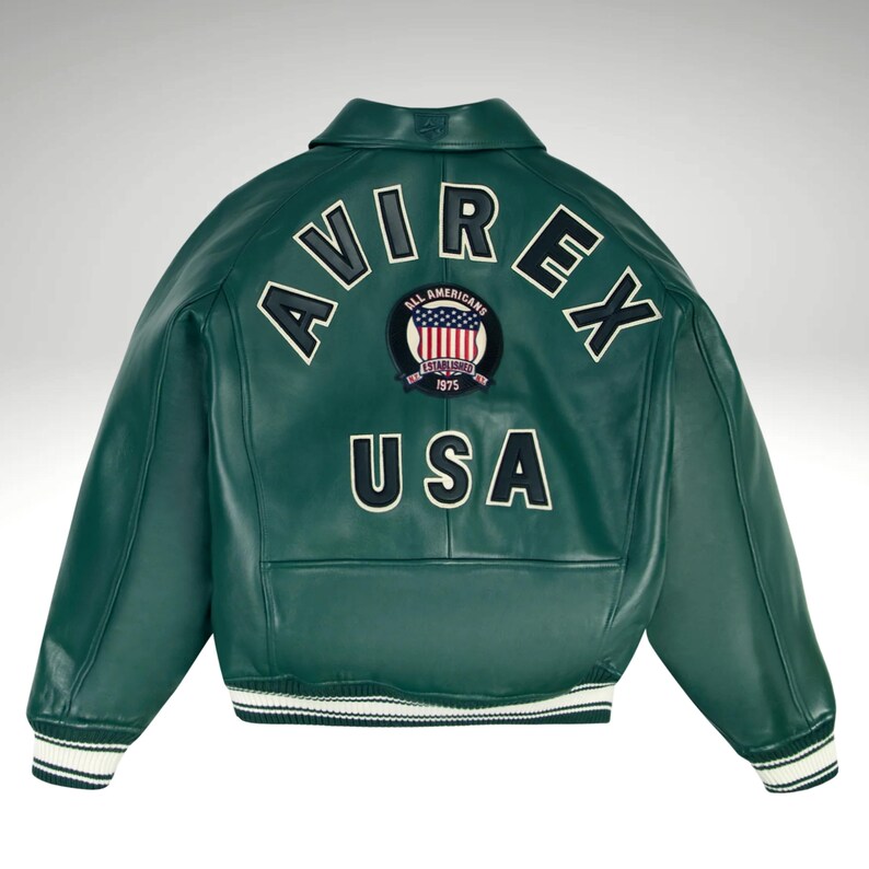 K&ouml;nnte beinhalten: Dunkelgr&uuml;ne Lederjacke mit dem Wort "AVIREX" in wei&szlig;en Buchstaben auf dem oberen R&uuml;cken. Darunter befindet sich ein Aufn&auml;her mit den Worten "All Americans" und "ESTABLISHED 1975". Das Wort "USA" ist darunter in Wei&szlig; gedruckt.