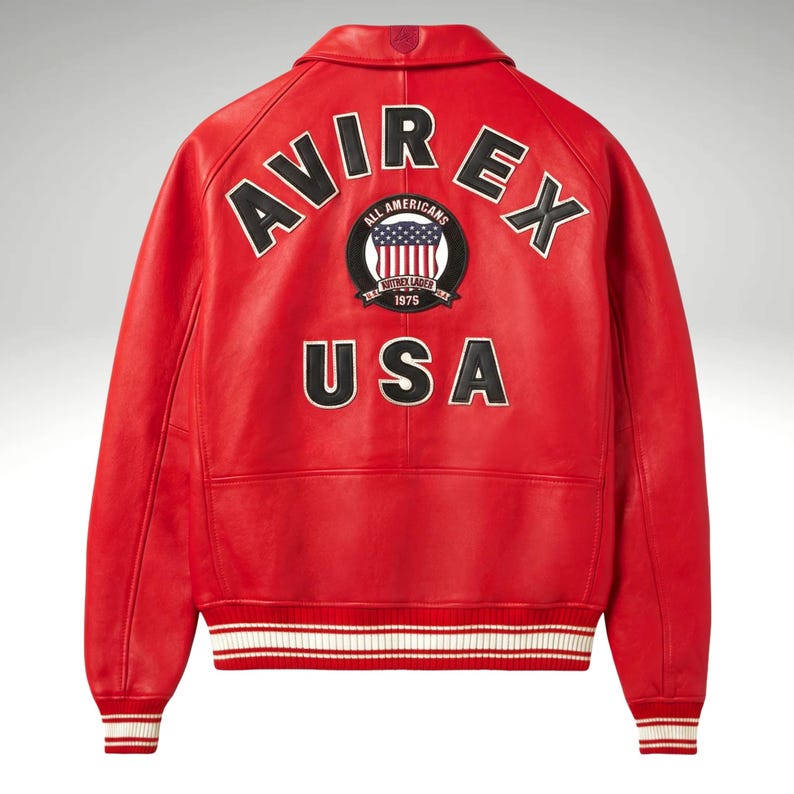 K&ouml;nnte beinhalten: Rote Lederjacke mit dem Wort "AVIREX" in wei&szlig;en Buchstaben &uuml;ber den Schultern. Ein kreisf&ouml;rmiger Aufn&auml;her mit den Worten "ALL AMERICANS" und "USA" ist ebenfalls sichtbar. Die Jacke hat wei&szlig;-rot gestreifte B&uuml;ndchen.