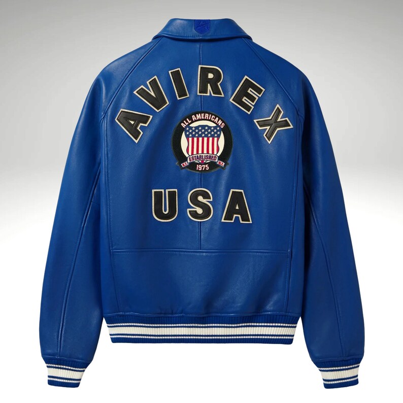 K&ouml;nnte beinhalten: Eine leuchtend blaue Lederjacke mit dem Wort "AVIREX" in schwarzen und wei&szlig;en Buchstaben &uuml;ber den Schultern. Darunter steht das Wort "USA". Ein kreisf&ouml;rmiger Aufn&auml;her mit der amerikanischen Flagge und den Worten "ALL AMERICANS ESTABLISHED 1975" ist zentriert.