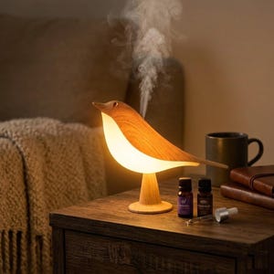 May include: A wooden bird-shaped essential oil diffuser with a warm, glowing light. The diffuser is on a wooden nightstand, with two small essential oil bottles and a dropper. Steam rises from the bird's beak.