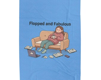 May include: A light blue blanket featuring a cartoon illustration of a person lounging on a tan sofa, holding a steaming mug. The text Flopped and Fabulous is printed above. Scattered around the sofa are a laptop, books, and papers.