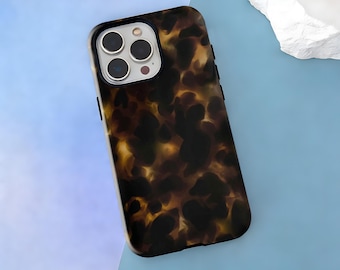May include: A tortoiseshell-effect phone case. The case features a dark brown and tan mottled pattern. The camera area has a black border with three camera lenses and a flash. The case is designed for a smartphone.