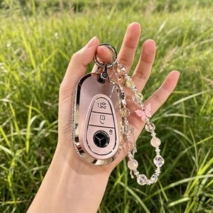 May include: A pink car key fob cover with a silver rhinestone border and a matching beaded keychain. The keychain features clear and pink beads, and a pink butterfly charm. The key fob has a silver key ring.