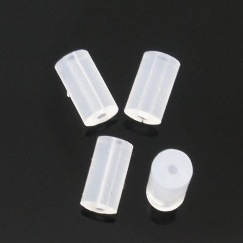 May include: Four small, cylindrical, translucent white silicone beads or spacers. Each piece features a smooth, matte-like finish and a central circular hole running through the length of the cylinder, providing a clear view of the opening.