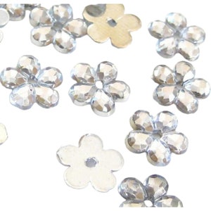 May include: A collection of silver-colored flower-shaped embellishments. The embellishments have a raised, faceted design and a hole in the center.