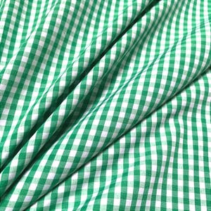 May include: Close-up of a green and white gingham fabric. The fabric is folded, showing the pattern's repeating squares. The green is a bright, spring-like hue, and the white provides contrast. This textile is suitable for various sewing projects.