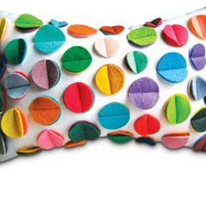 K&ouml;nnte beinhalten: Ein wei&szlig;es rechteckiges Kissen mit bunten Filzkreisen, die auf die Vorderseite gen&auml;ht sind. Die Kreise sind in verschiedenen Schattierungen von Rot, Orange, Gelb, Gr&uuml;n, Blau, Lila und Rosa.